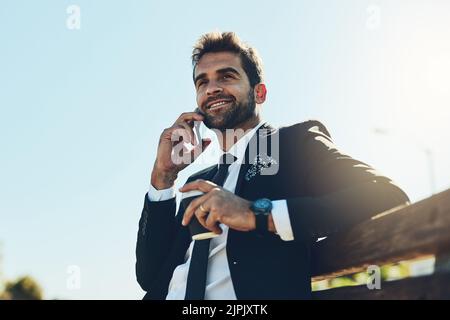 Eine Pause vom Büro und draußen arbeiten. Ein hübscher junger Geschäftsmann auf einem Anruf in einem öffentlichen Park. Stockfoto