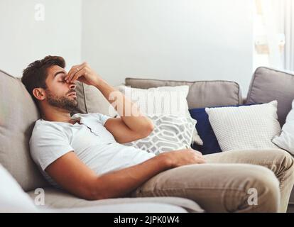 Heute gehe ich nirgendwo hin. Ein hübscher junger Mann hält seine Nase, während er tagsüber auf einer Couch zu Hause liegt. Stockfoto