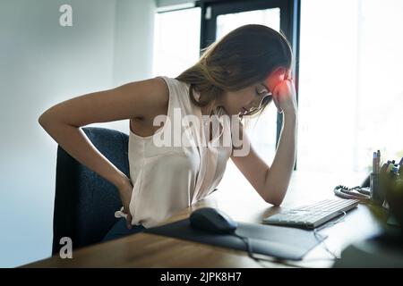 Das Gefühl der Schmerzen am ganzen Körper. Eine junge Geschäftsfrau, die unter Kopfschmerzen und Rückenschmerzen leidet, während sie in einem Büro arbeitet. Stockfoto