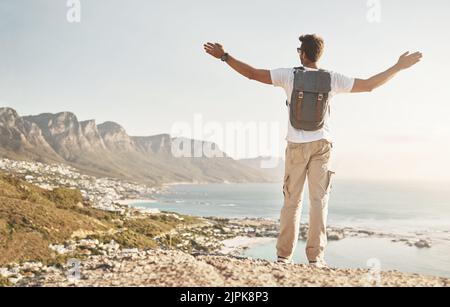 Spüren Sie die Freiheit. Rückansicht eines nicht erkennbaren jungen Mannes, der mit ausgestreckten Armen in den Bergen unterwegs war. Stockfoto