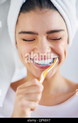 Sie werden sehen, wie sie funkeln, wenn ich fertig bin. Eine schöne junge Frau putzt sich ihre Zähne im Badezimmer zu Hause. Stockfoto