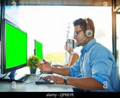 Das beste Team, um Ihre Fragen zu behandeln. Ein junger Mann und eine junge Frau, die Computer mit grünen Bildschirmen in einem Callcenter verwenden. Stockfoto