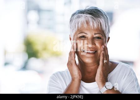 Sie hat einen natürlichen Glanz. Porträt einer fröhlichen reifen Frau, die ihr Gesicht mit den Händen hält, während sie auf die Kamera schaut. Stockfoto