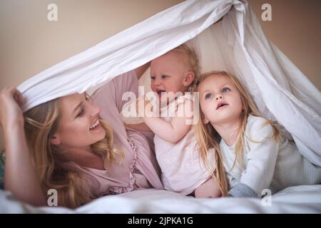 Familie, der Schlüssel zum Glück. Eine entzückende dreiköpfige Familie, die zu Hause unter einem Laken auf dem Bett spielt. Stockfoto