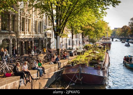 Junge Leute entspannen sich mit Reihenhäusern und Hausbooten entlang der Prinsengracht, Amsterdam, Holland Stockfoto