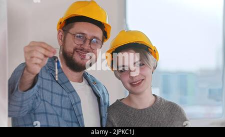 Glückliche, schwanger Frau mit ihrem Mann, der Schlüssel aus der neuen Wohnung hat. Mittlerer Schuss Stockfoto