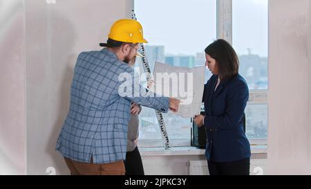 Ein Immobilienmakler zeigt ein Layout für ein junges Ehepaar - diskutieren. Mittlerer Schuss Stockfoto