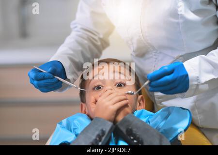 Wie komme ich aus dem raus? Ein verängstigter kleiner Junge, der sich auf einen Zahnarztstuhl legt und seinen Mund geschlossen hält, um den Zahnarzt von der Arbeit abzuhalten Stockfoto