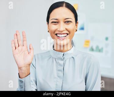 Frau winkt mit der Hand, um Hallo zu begrüßen, während sie während eines Videoanrufs über die Webcam in einem virtuellen Meeting in einem Büro vorstellt, lächelt und gestikelt. Porträt eines Stockfoto