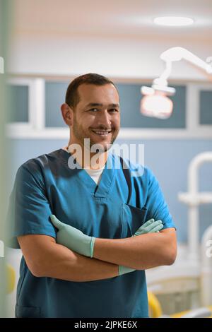 Er wird dafür stehen, dass Sie jeden Tag ein strahlendes Lächeln haben. Porträt eines fröhlichen jungen Zahnarztes, der mit gefalteten Armen steht, während er die anschaut Stockfoto