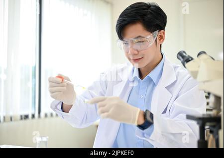 Ein intelligenter und talentierter junger asiatischer Wissenschaftler, der sich konzentriert, passt eine Virusprobe in einer Petrischale in seinem Wissenschaftslabor an. Stockfoto