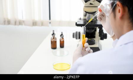 Talentierter junger asiatischer Wissenschaftler, der in seinem Wissenschaftslabor eine flüssige chemische Probe in einem Reagenzglas anpasst. Nahaufnahme Stockfoto