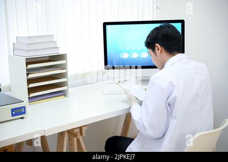 Ein professioneller asiatischer Arzt am Schreibtisch seines Büros in der Arztpraxis, der einen medizinischen Bericht oder eine Medikamentenhistorie seines Patienten auf dem untersucht Stockfoto