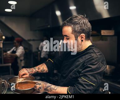 Einige letzte Minute Anpassungen für Geschmack. Ein fokussierter Koch bereitet ein Gericht in der Küche eines Restaurants. Stockfoto