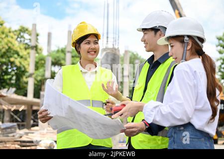 Zwei professionelle asiatische weibliche und männliche Architekten arbeiten, betrachten die Blaupause und inspizieren das Gebäude mit einer weiblichen Bauinspektion Stockfoto