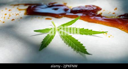 Starker Cannabisextrakt aus Goldwachs mit hohem thc-Gehalt und grünem Marihuanablatt auf Papier aus nächster Nähe. Stockfoto