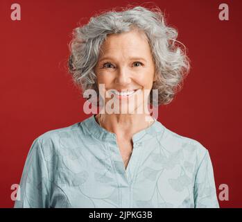 . Porträt einer älteren, fröhlichen und fröhlichen Frau, die vor einem roten Hintergrund im Studio steht. Reife Frau mit gesunden, weißen und sauberen Zähnen zeigt orale Stockfoto
