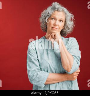 Reife Frau denkt, eine Entscheidung oder Wahl darüber, was mit Copy Space zu tragen. Verwirrte ältere kaukasische Frau verlor in ihren Gedanken. Ernst Stockfoto
