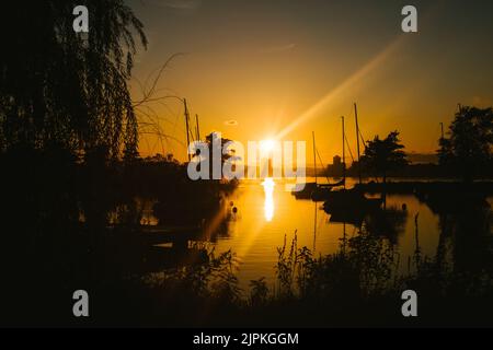 Sonnenuntergang mit goldenen Strahlen über Booten im Hafen Stockfoto