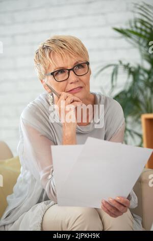 Nachdenkliche, hübsche ältere Frau mit Geschäftsdokumenten Stockfoto
