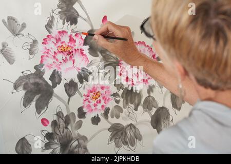Ältere Frau malt schöne Blumen, Blick von hinten Stockfoto