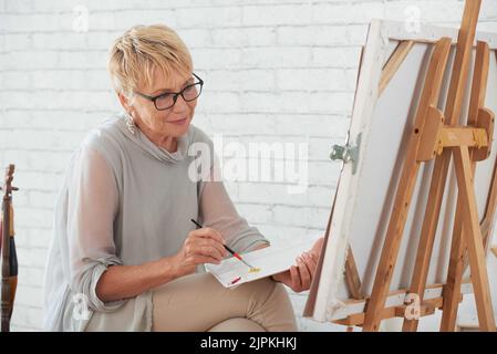 Ältere Frau Malerei auf Leinwand in Home Studio Stockfoto