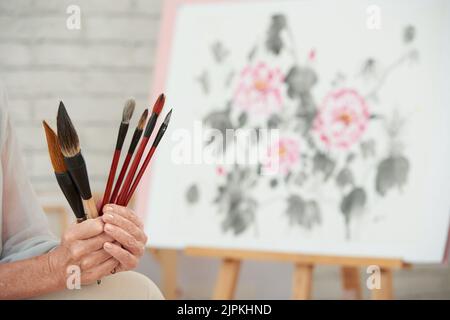 Set von Bürsten in den Händen der älteren Malerin Stockfoto