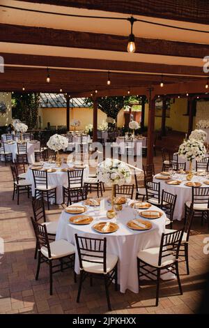Wunderschöne Außenrezeptionsstätte - weiße Tischdecken, goldene Teller, weiße Rosen in den Mittelpunkt Stockfoto