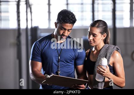 Trainer, der Training, Zeitplan und Training mit dem Athleten für aktiv, Fitness und Wellness in einem Fitnessstudio plant. Trainer schreibt Notizen für Sportkunden mit Stockfoto