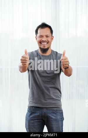Fröhlicher asiatischer Mann mit Daumen nach oben und Blick auf die Kamera Stockfoto