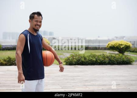 Porträt eines fröhlichen philippinischen Mannes, der im Freien Basketball spielt Stockfoto