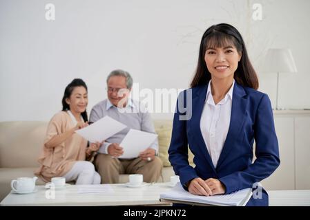 Porträt einer ziemlich lächelnden vietnamesischen Immobilienmaklerin und ihrer älteren Kundin im Hintergrund Stockfoto