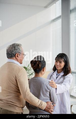 Lächelnd hübsche Ärztin, die das gealterte Paar beruhigt Stockfoto