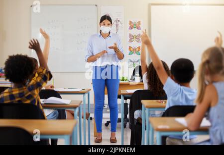 Der Lehrer stellt Schulkinder Fragen, die eifrig, intelligent und klug für die Bildung in einer covid Pandemie sind. Studenten heben die Hand, um sich freiwillig zu melden, und beizutreten Stockfoto