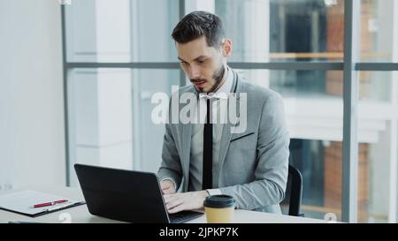 Ein junger Geschäftsmann, der einen Laptop verwendet, sitzt im modernen Büro im Innenbereich Stockfoto