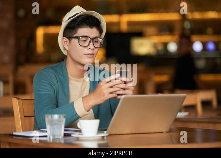 Hübscher junger asiatischer Mann, der Nachrichten auf seinem Smartphone liest Stockfoto