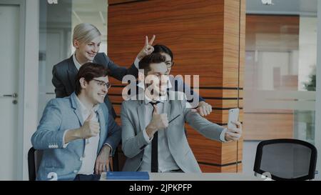 Glückliches Geschäftsteam, das Selfie-Portraits auf der Smartphone-Kamera macht und während des Meetings in modernen Büros in Innenräumen für Gruppenfotos posiert Stockfoto