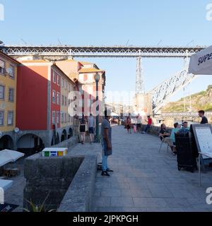 Gäste speisen in einem Restaurant im Ribeira aka Riverside Viertel von Porto mit einem Restaurantmitarbeiter im Vordergrund und der Luis I Brücke im Hintergrund. Stockfoto