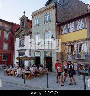 Menschen genießen einen Sommerabend neben einem Restaurant, einer Kirche und charaktervollen Gebäuden im Ribeira aka Riverside Viertel von Porto. Portugal. Stockfoto