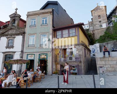 Menschen genießen einen Sommerabend neben einem Restaurant, einer Kirche und charaktervollen Gebäuden im Ribeira aka Riverside Viertel von Porto. Portugal. Stockfoto