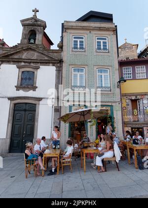 Menschen genießen einen Sommerabend neben einem Restaurant, einer Kirche und charaktervollen Gebäuden im Ribeira aka Riverside Viertel von Porto. Portugal. Stockfoto