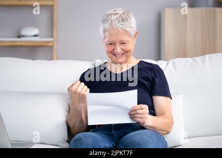 Lächelnde Frau Beim Lesen Des Briefes, Während Sie Zu Hause Auf Dem Sofa Sitzt Stockfoto