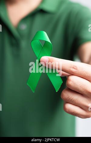 Grünes Farbband mit der Hand für Leber, Gallenleiter, Gallengang, Gebärmutterhalskrebs, Nierenkrebs und Lymphom-Bewusstsein. Gesundheitswesen und Weltkrebstag CO Stockfoto