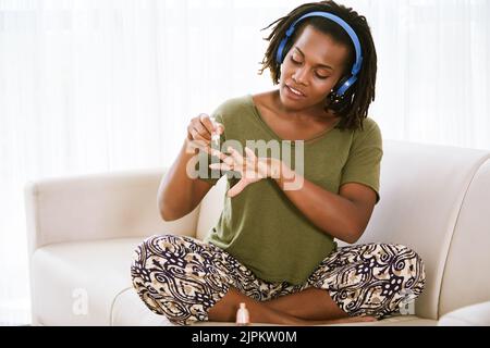 Afroamerikanische Frau mit Kopfhörern, die zu Hause Maniküre macht Stockfoto