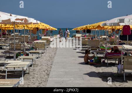 Blick auf den italienischen Strand mit Sonnenschirmen und Sonnenliegen. Weißer Wanderweg. Riviera Romagnola, Italien Stockfoto