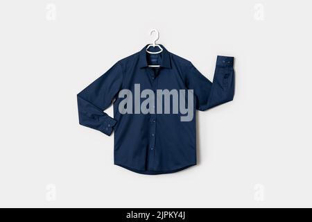 Die Vorderansicht eines dunkelblauen Button-Down-Shirts auf einem Hemdaufhänger, isoliert auf weißem Hintergrund. Hochwertige Fotos Stockfoto