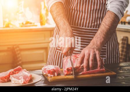 Man schneidet von frischem Stück Rindfleisch auf einer hölzernen Schneidebrett in der Küche zu Hause Stockfoto