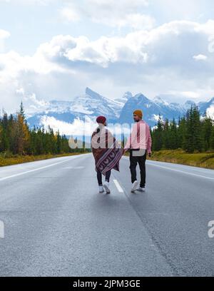 Icefields Parkway mit Herbstbäumen und schneebedeckten, nebligen Bergen in Jasper Canada, Alberta. Ein Paar Männer und Frauen, die auf einer asphaltierten Straße am Icefield parkway spazieren Stockfoto