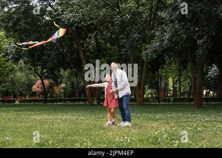 Fröhliche asiatische Familie, die im Sommerpark fliegende Drachen ansieht Stockfoto