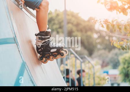 Nahaufnahme der Beine eines Rollers, der Tricks ausführt und einfach nur auf der Rampe im städtischen Sportpark fährt. Teenager-Hobby-Konzept Stockfoto
